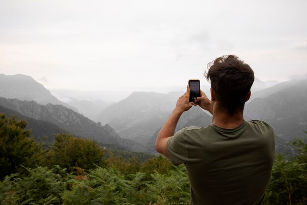 Jonge mannelijke reiziger die een foto van de bergen maakt met zijn smartphone