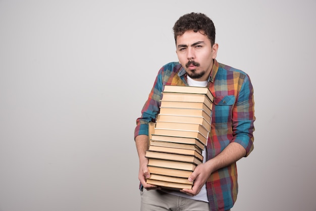 Jonge mannelijke student die met stapel boeken camera bekijkt.