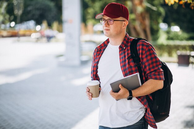 Jonge mannelijke student het drinken koffie met laptop in park