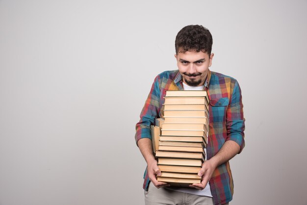 Jonge mannelijke student met stapel boeken poseren voor de camera.