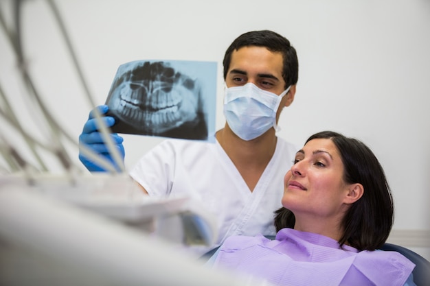 Jonge mannelijke tandarts die Röntgenstraal met de vrouwelijke patiënt onderzoekt
