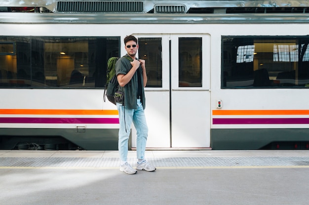 Gratis foto jonge mannelijke toerist met rugzak het stellen bij station