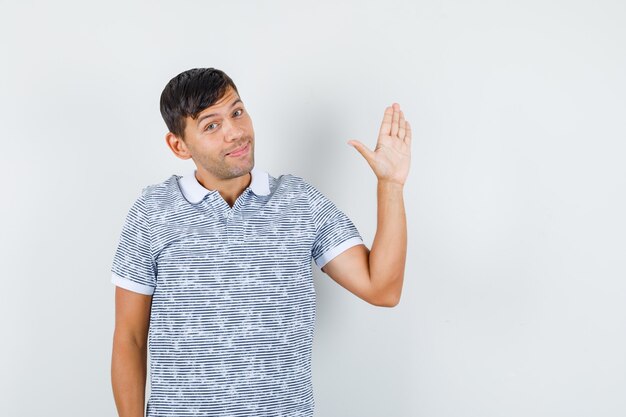 Jonge mannelijke zwaaiende hand om afscheid te nemen in t-shirt en op zoek blij
