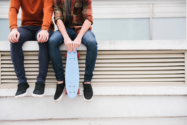 Jonge mannen zitten op hek met longboard