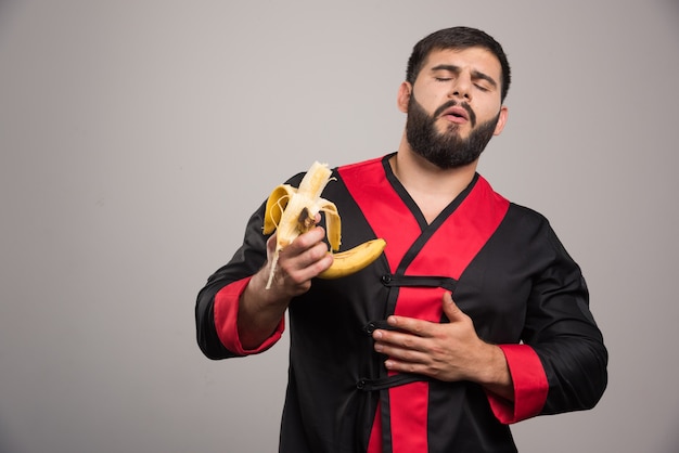 Jonge mens die een banaan op grijze muur eet.