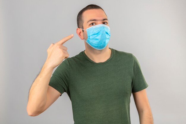 Jonge mens die gezichts medisch masker draagt dat aan zich met vinger op geïsoleerd wit richt