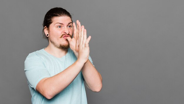 Jonge mens die het gebaar van de handtrompet tegen grijze achtergrond maakt