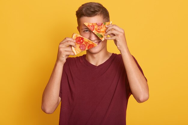 Jonge mens die twee stukken van heerlijke pizza in zijn handen houdt en zijn ogen behandelt met smakelijk product