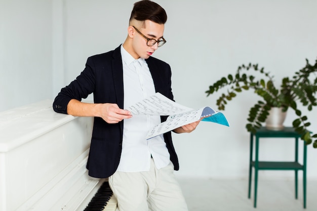 Gratis foto jonge mens die zich dichtbij de piano bevindt die muzikaal blad bekijkt