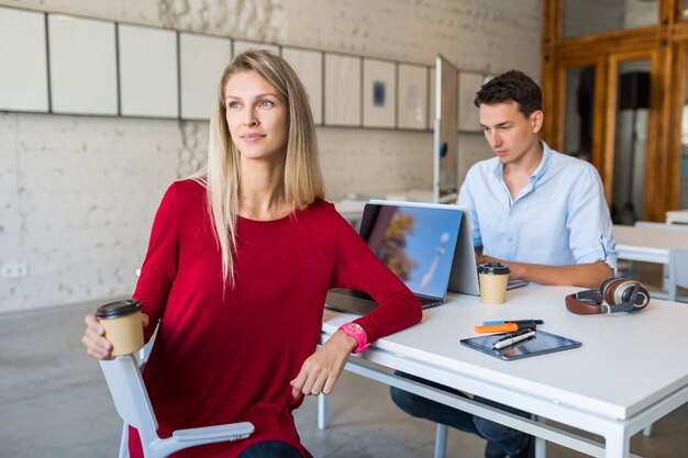 Jonge mensen zitten aan tafel, werken op laptop in co-working office