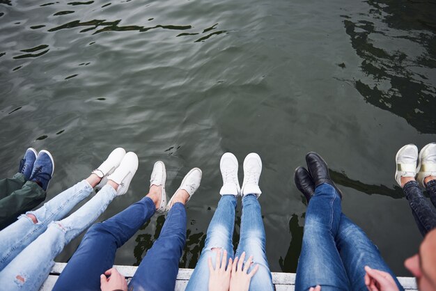 Jonge mensenvrienden die op de rivierbrug, levensstijl, voeten over blauw water zitten.