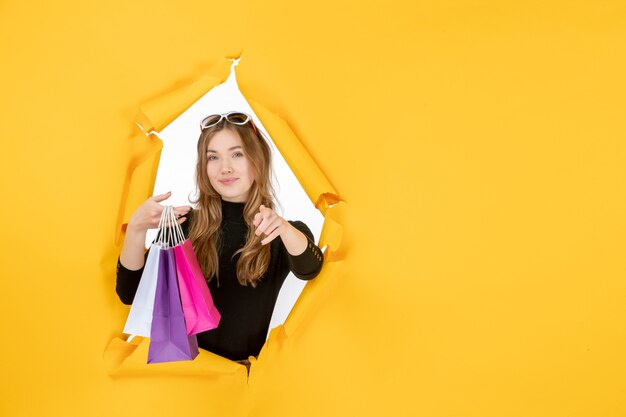 Jonge mode vrouw met boodschappentassen door gescheurd papier gat in de muur