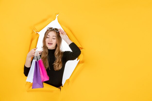 Jonge mode vrouw met boodschappentassen door gescheurd papier gat in de muur