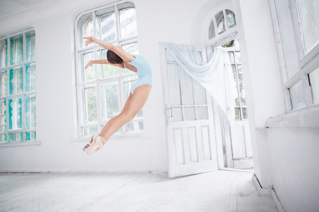 Jonge moderne balletdanser die op witte muur springt