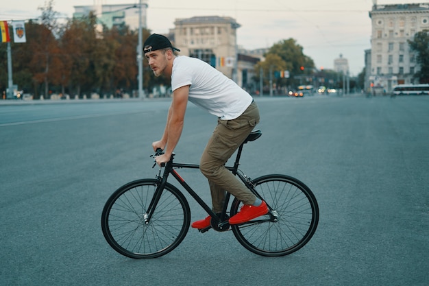 Jonge moderne man fietsen op een klassieke fiets op de stadsweg