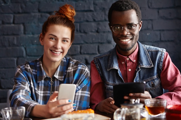 Jonge moderne mensen met elektronische apparaten plezier tijdens koffiepauze binnenshuis in café.