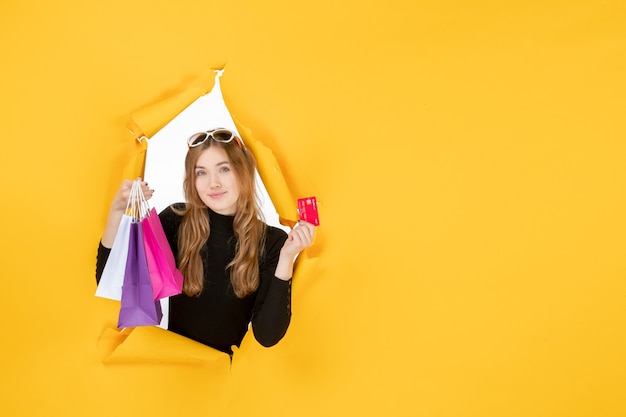 Jonge modevrouw met boodschappentassen en creditcard door een gescheurd papiergat in de muur