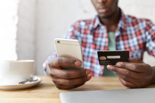 jonge modieuze kerel zit in een café met smartphone en laptop