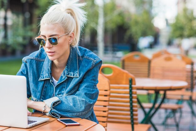 Jonge modieuze vrouw met behulp van laptop in de open lucht