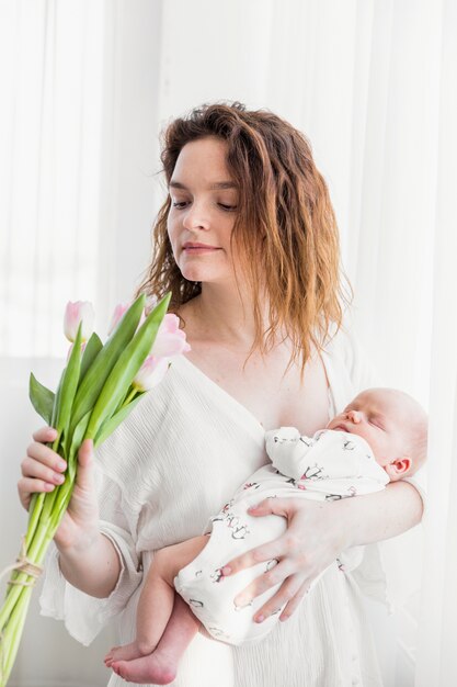 Jonge moeder die haar baby met roze tulpenbloemen vervoert