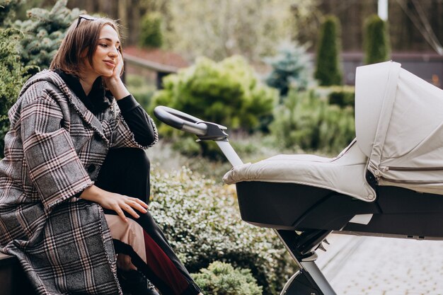 Jonge moeder die met kinderwagen in de achtertuin lopen