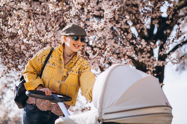 Jonge moeder die met kinderwagen in park loopt