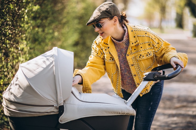 Jonge moeder die met kinderwagen in park loopt