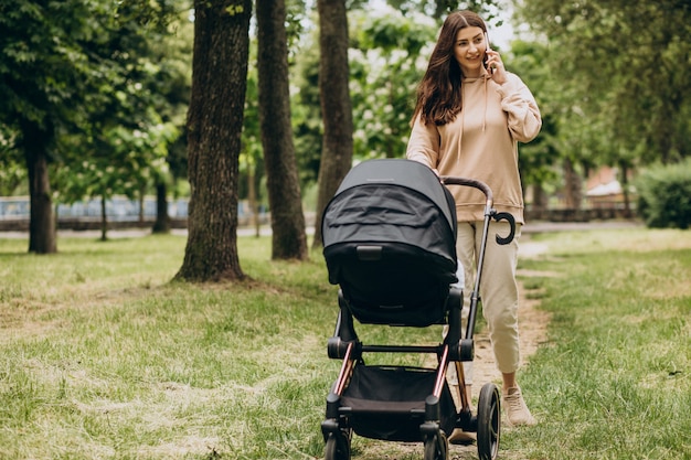 Jonge moeder die met kinderwagen in park loopt