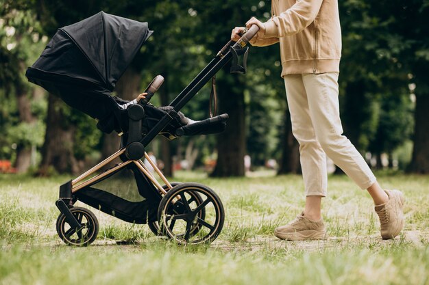 Jonge moeder die met kinderwagen in park loopt