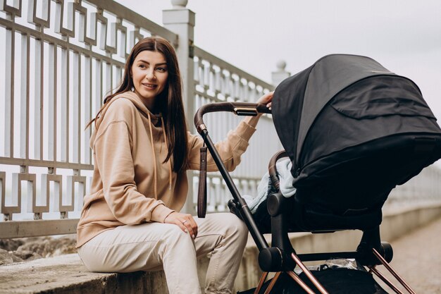 Jonge moeder die met kinderwagen in park loopt