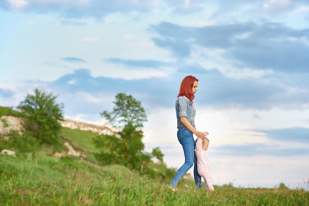 Jonge moeder die op het veld loopt en de handen van haar dochtertje vasthoudt