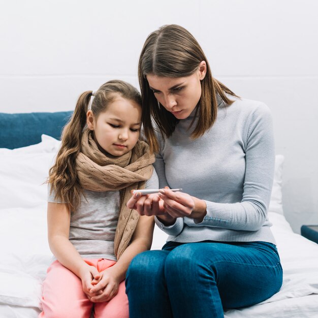 Jonge moeder die temperatuur van haar zieke dochter op thermometer toont