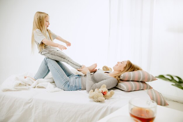 Jonge moeder en haar dochtertje thuis op zonnige ochtend. Zachte pastelkleuren. Gelukkige familietijd in het weekend. Moederdag concept. Concepten voor familie, liefde, levensstijl, moederschap en tedere momenten.