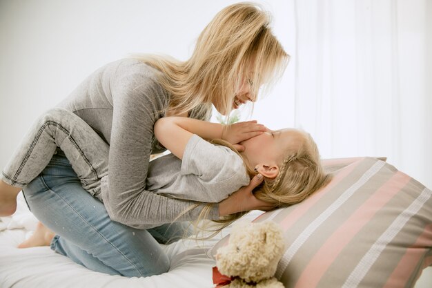 Jonge moeder en haar dochtertje thuis op zonnige ochtend. Zachte pastelkleuren. Gelukkige familietijd in het weekend. Moederdag concept. Concepten voor familie, liefde, levensstijl, moederschap en tedere momenten.