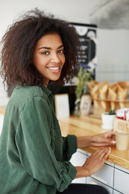 Jonge mooie afrikaanse studentezitting in koffie het glimlachen het drinken koffie.