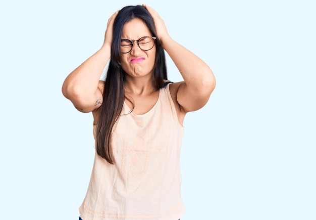 Jonge, mooie blanke vrouw, gekleed in casual kleding en een bril die lijdt aan hoofdpijn, wanhopig en gestrest vanwege pijn en migraine. handen op het hoofd.