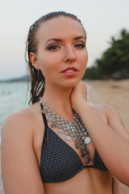 Jonge mooie blonde vrouw die op zandstrand in bikini zwemmend kostuum, uitstekende halsband zonnebaden