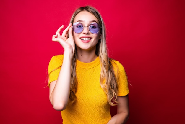 Jonge mooie blonde vrouw met zonnebril geïsoleerd op rode muur