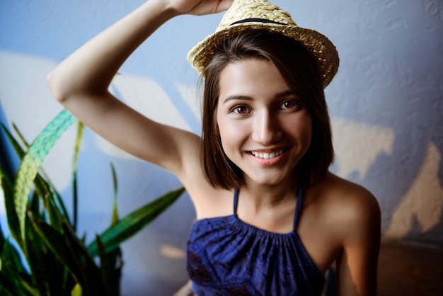 Jonge mooie brunette meisje in hoed zittend op trappen, glimlachend.