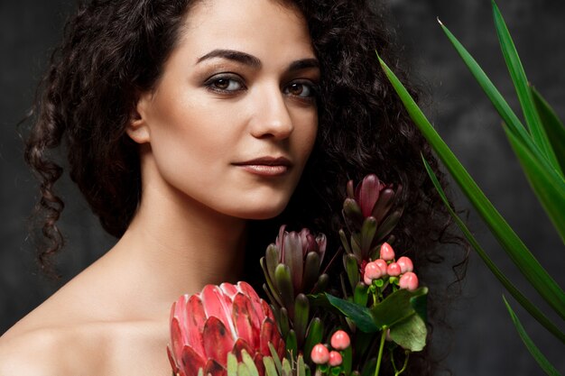 Jonge mooie brunette meisje in tropische planten over grijze muur