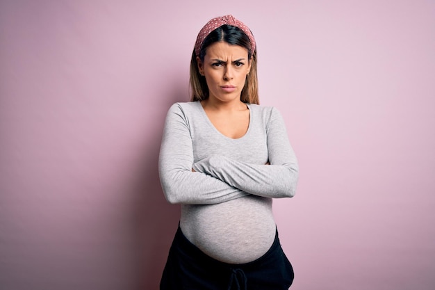 Jonge mooie brunette vrouw zwanger verwacht baby over geïsoleerde roze achtergrond scepticus en nerveus afkeurende uitdrukking op gezicht met gekruiste armen negatieve persoon