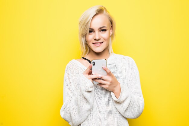 Jonge mooie dame vrouw meisje in witte trui maakt gebruik van smartphone op geel