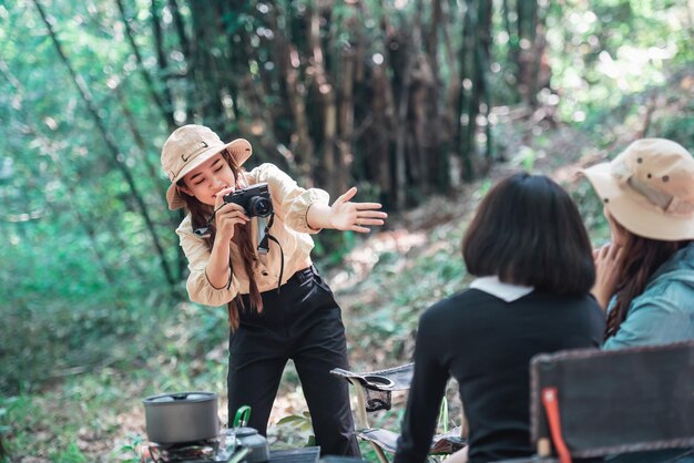 Jonge mooie foto nemen door camera twee vrouwelijke vrienden terwijl ze in de campingtent in het bos zitten op vakantievakantie Jonge Aziatische groepsvrouw reizen buiten kamperen