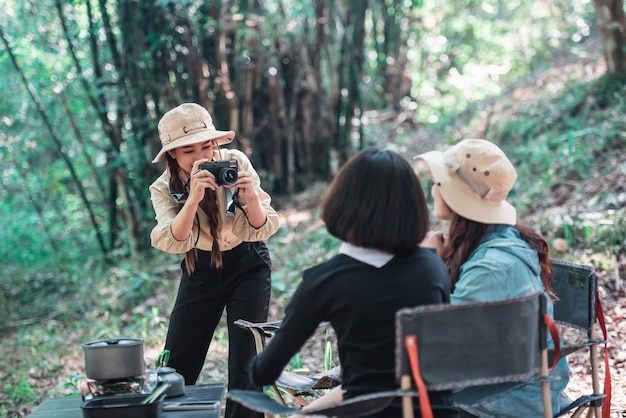 Jonge mooie foto nemen door camera twee vrouwelijke vrienden terwijl ze in de campingtent in het bos zitten op vakantievakantie jonge aziatische groepsvrouw reizen buiten kamperen