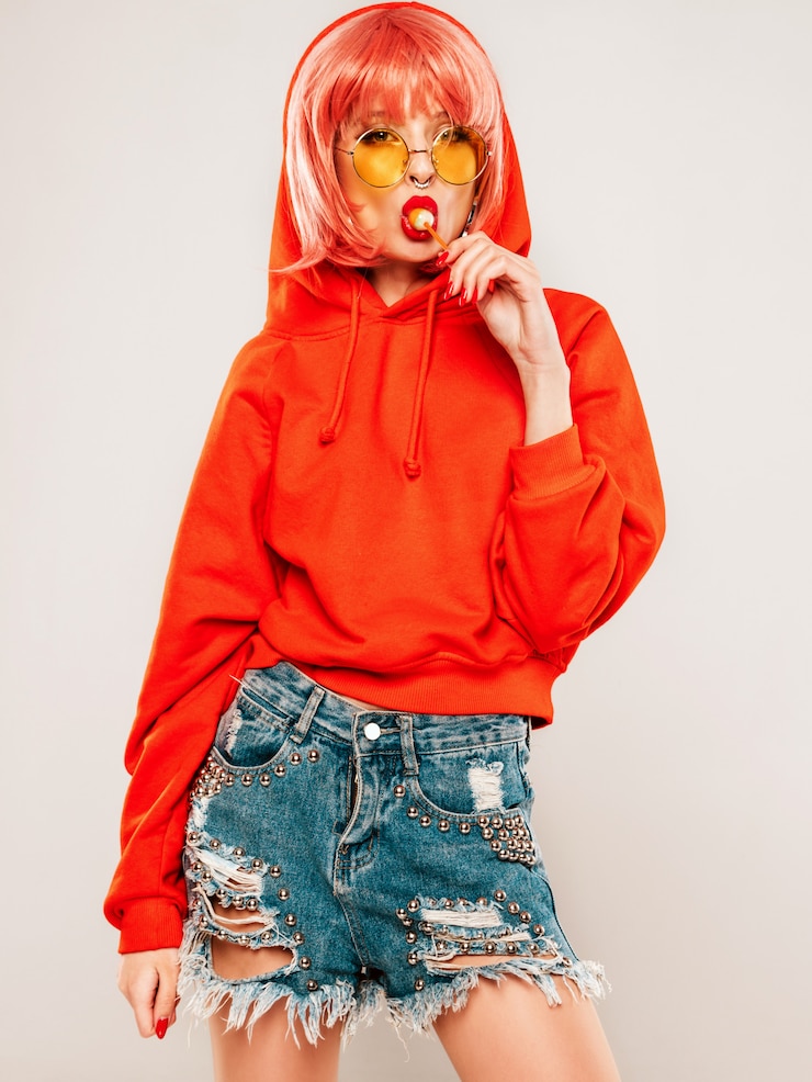 Gratis Foto jonge mooie hipster slecht meisje in trendy rode zomer rode hoodie en oorbel in haar neus. sexy zorgeloze vrouw poseren in studio op grijze achtergrond in pruik. heet model likken rond suikersuikergoed