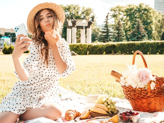 Jonge mooie hipster vrouw in trendy zomerjeans, roze T-shirt en hoed. Zorgeloze vrouw die buiten picknick maakt.