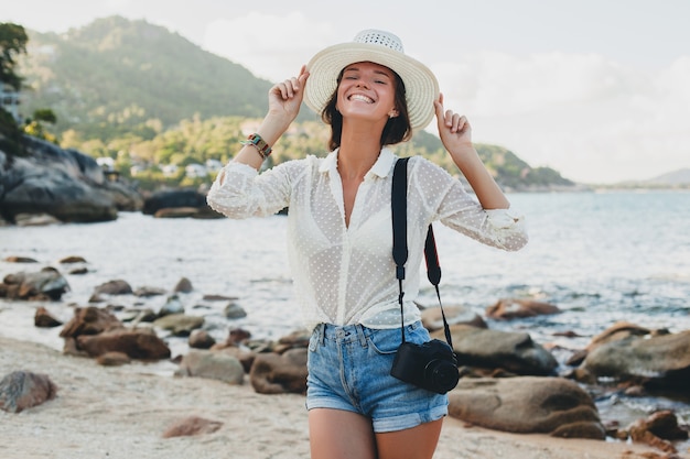 Jonge mooie hipster vrouw op zomervakantie in Azië, ontspannen op tropisch strand, digitale fotocamera, casual boho-stijl, zee landschap, slank gebruind lichaam, alleen reizen