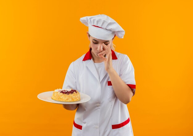 Jonge mooie kok in chef-kok uniform houden en plaat van cake kijken en lekker gebaar doen