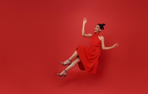 Jonge mooie lachende aziatische vrouw rode jurk zwevend in de lucht ontspannen geïsoleerd op rode achtergrond