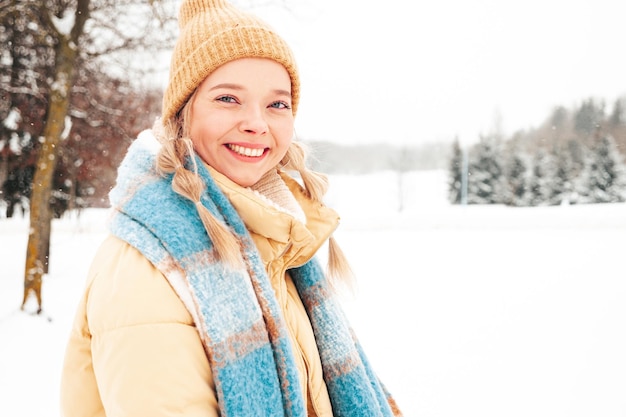 Jonge mooie lachende hipster vrouw in trendy warme kleding en sjaal. zorgeloos vrouw poseren in de straat in het park. positief puur model met plezier in de sneeuw. genieten van winterse momenten